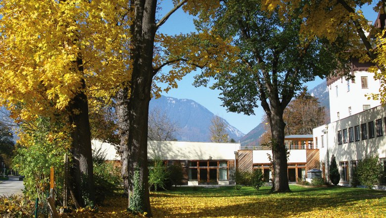 Herbstszene mit Hotelgebäude und gelben Blättern auf dem Boden.