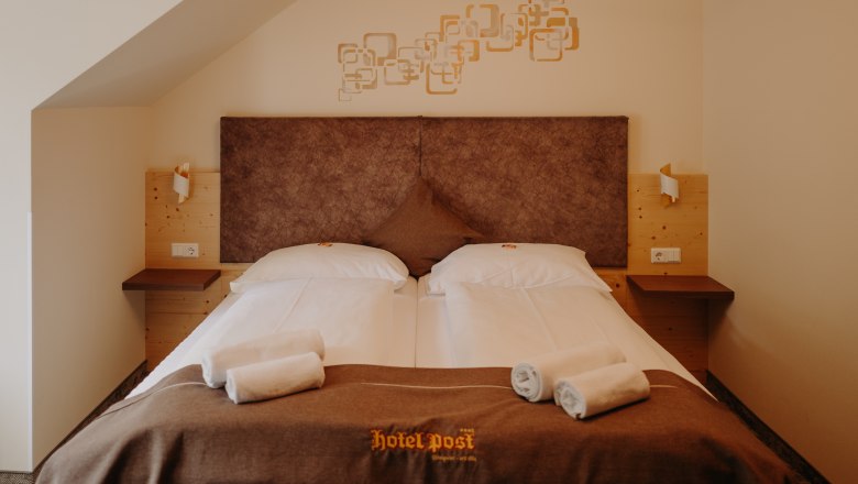 Gem&uuml;tliches Hotelzimmer mit Doppelbett, mit heller Holzverkleidung und erdigen Farbt&ouml;nen.
