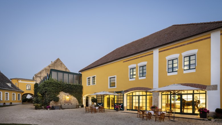Gelbes Geb&auml;ude mit Innenhof und Tischen im Freien bei D&auml;mmerung.