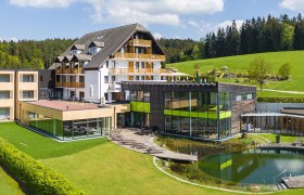 Hotel Schwarz Alm mit modernem Design, umgeben von gr&uuml;ner Landschaft und Wald.
