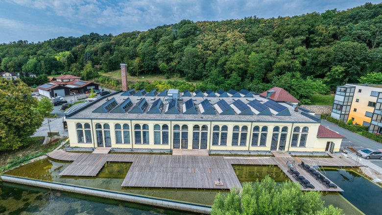 Luftaufnahme einer alten Fabrik mit Solarpanelen auf dem Dach, umgeben von B&auml;umen und einem Teich.