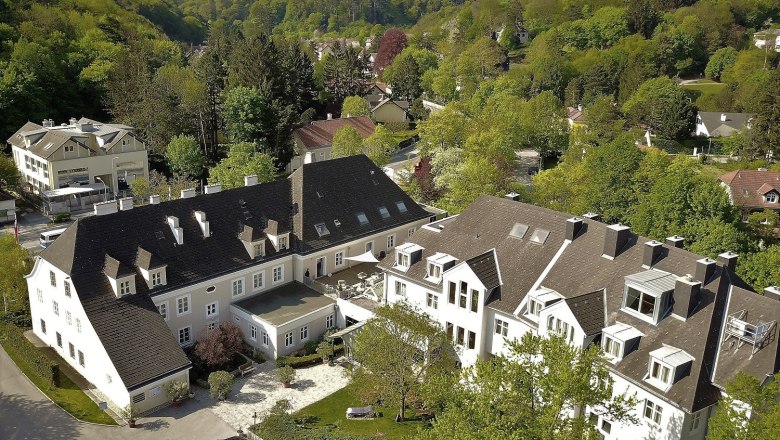 Luftaufnahme eines großen Gebäudekomplexes umgeben von grünen Bäumen und Hügeln.