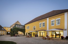 Gelbes Gebäude mit Innenhof und Tischen im Freien bei Dämmerung.