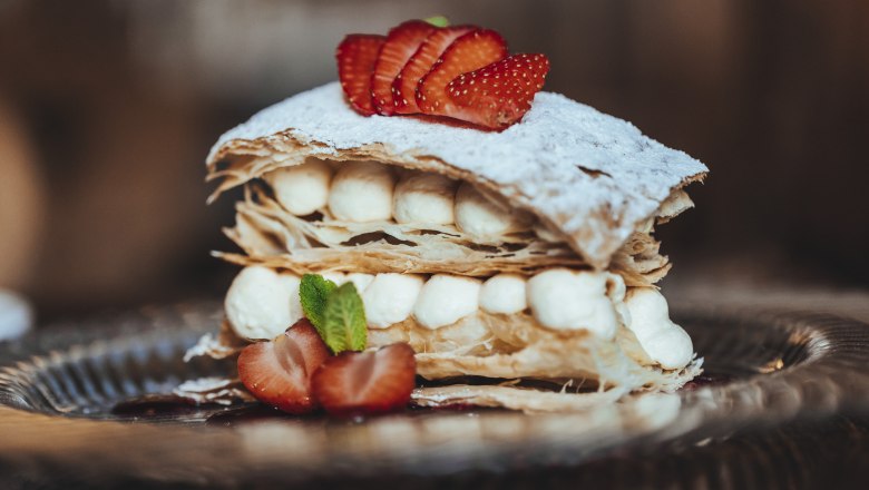 Eine Cremeschnitte mit Bl&auml;tterteig, Sahne und Erdbeeren auf einem Teller.