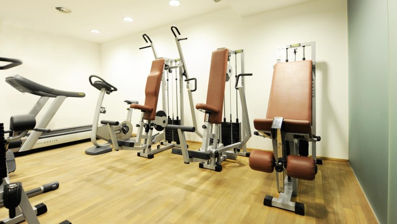 Ein Fitnessraum mit Laufband, Heimtrainer und Kraftgeräten auf Holzboden.