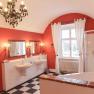 Elegantes Badezimmer mit roten W&auml;nden, zwei Waschbecken, Badewanne, Dusche und Kronleuchter.