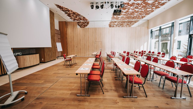 Innenansicht eines modernen Konferenzraums mit roten Stühlen und Holzboden.
