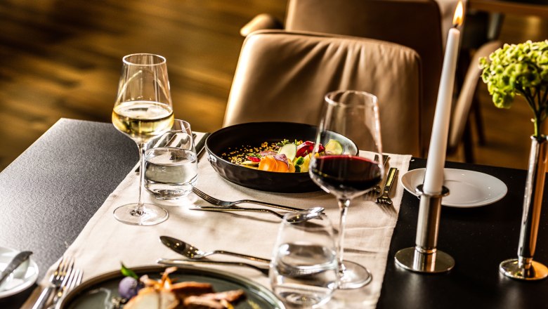 Eleganter Restauranttisch mit Weingl&auml;sern, Kerze und Gourmetgerichten.