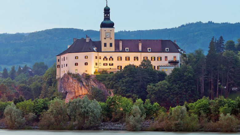 Schloss Persenbeug auf einem H&uuml;gel mit Fluss im Vordergrund.