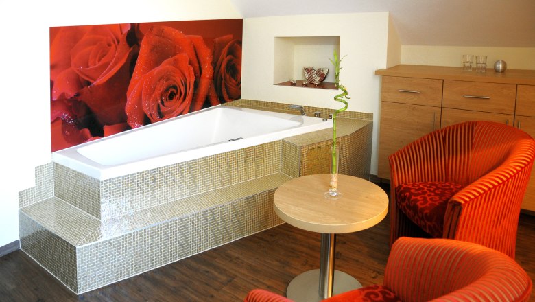 Gem&uuml;tliches Zimmer mit Badewanne, roten Sesseln und Rosenbild an der Wand.