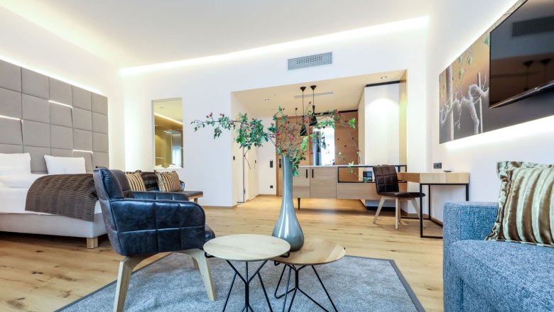 Modern eingerichtetes Hotelzimmer mit Bett, Sesseln, Tisch und Dekoration.