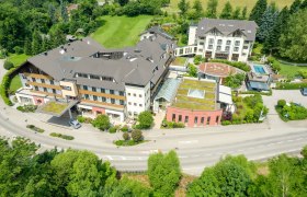 Luftaufnahme eines gro&szlig;en Hotelkomplexes mit mehreren Geb&auml;uden, umgeben von gr&uuml;ner Landschaft.