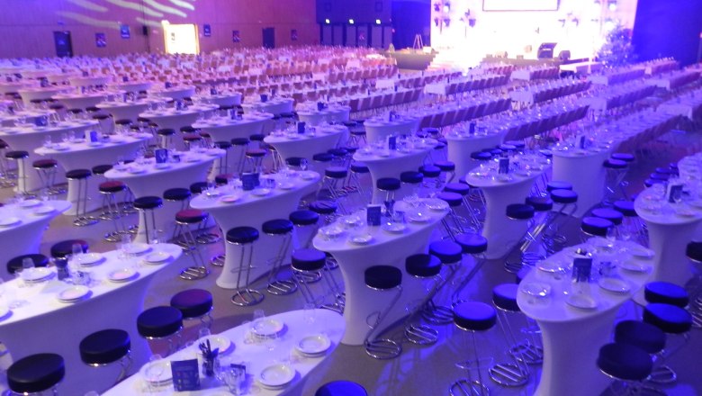 Großer Saal mit gedeckten Tischen und Stühlen, beleuchtet in Blau und Lila.