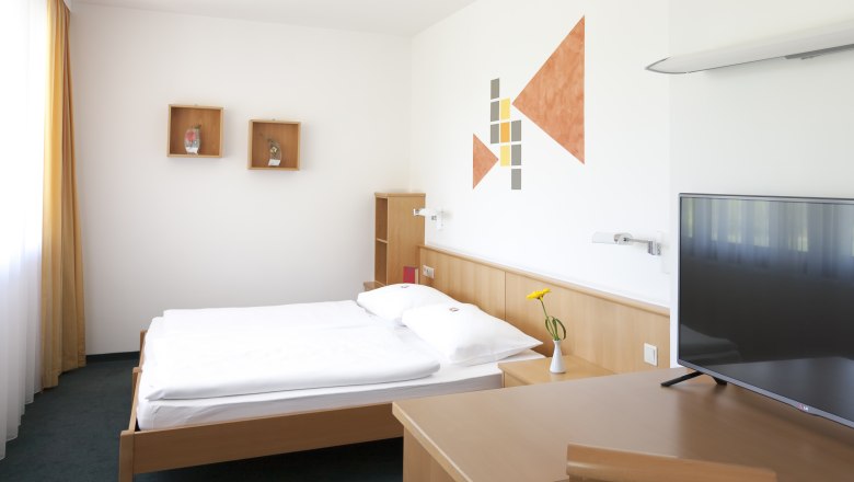 Modern eingerichtetes Hotelzimmer mit Bett, Schreibtisch, Fernseher und Wanddekoration.