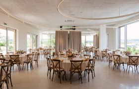 Eleganter Veranstaltungsraum mit runden Tischen, St&uuml;hlen und Blumendekoration.