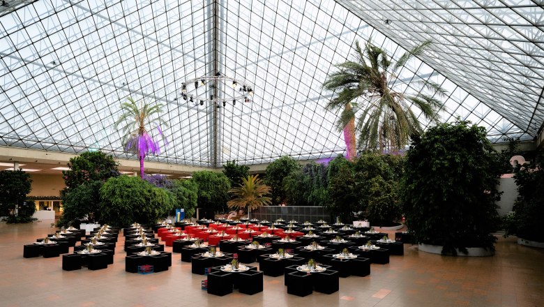 Innenansicht der Eventpyramide mit gedeckten Tischen und Palmen unter einem Glasdach.