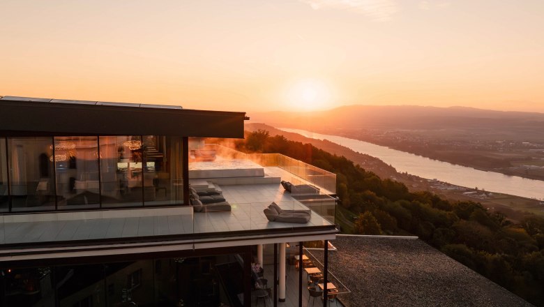 Modernes Hotel mit Terrasse und Flussblick bei Sonnenuntergang und Blick &uuml;ber die Donau.