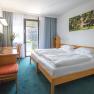 Hotelzimmer mit Doppelbett, Schreibtisch, Stuhl und Balkon.