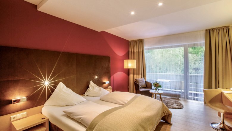 Modernes Hotelzimmer mit Doppelbett, roter Wand, gro&szlig;em Fenster und Sitzbereich.