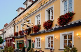 Fassade eines gelben Gebäudes mit dem Schriftzug 'Hotel-Restaurant zur Post'. Vor dem Gebäude sitzen Menschen an Tischen.