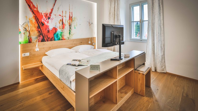 Modernes Hotelzimmer mit Doppelbett, abstraktem Kunstwerk an der Wand und einem Fernseher auf einem Regal.