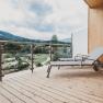 Holzterrasse mit Liegestuhl und Blick auf gr&uuml;ne Landschaft und Berge.
