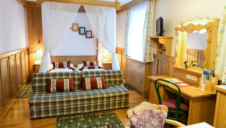 Gemütliches Hotelzimmer mit Doppelbett, Sofa, Schreibtisch und Spiegel in rustikalem Stil.