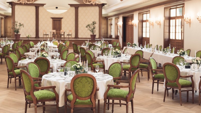 Eleganter Festsaal mit gedeckten Tischen und grünen Stühlen im Schloss Thalheim.