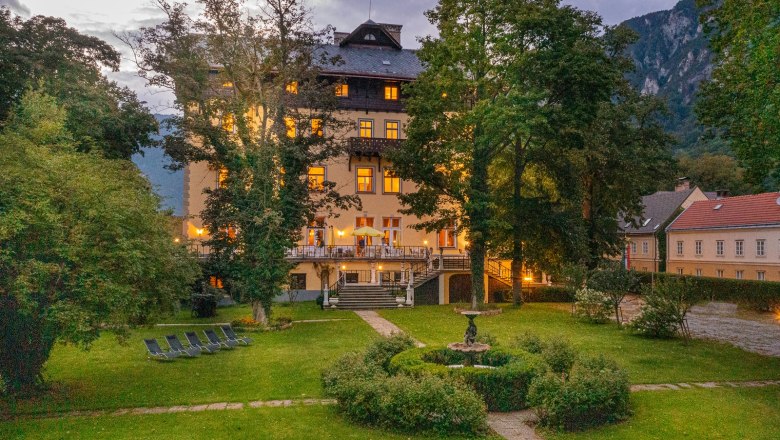 Ein beleuchtetes Gebäude mit Garten und Liegestühlen bei Dämmerung.