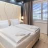 Modernes Hotelzimmer mit Doppelbett, roten Sesseln und gro&szlig;en Fenstern mit Vorh&auml;ngen.