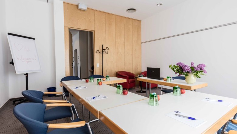 Konferenzraum mit Tischen, Stühlen, Flipchart und Blumen.