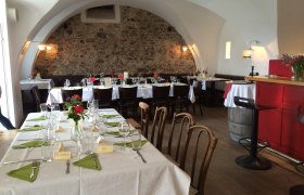 Gemütlicher Gastraum mit gedeckten Tischen, Steinwand und gewölbter Decke.