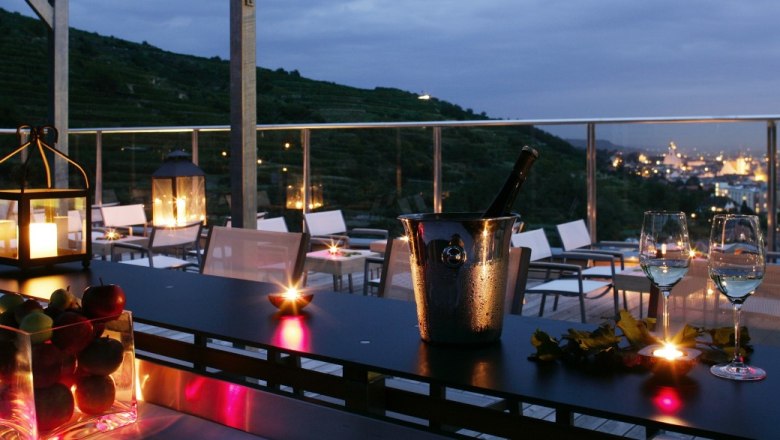 Abendliche Terrasse mit Kerzenlicht, Weingl&auml;sern und Blick auf eine Stadt.