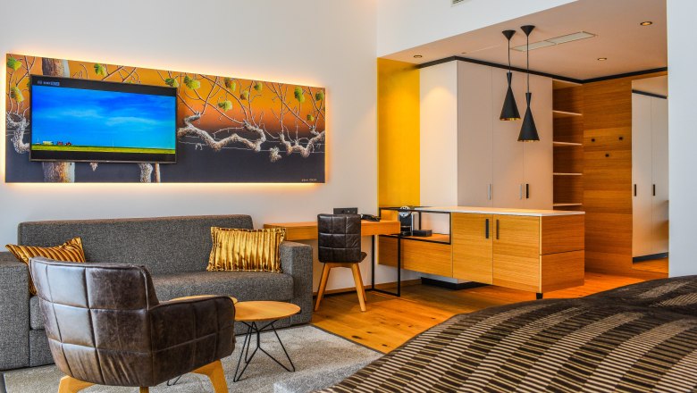 Moderne Hotelsuite mit Sofa, Sessel, TV und Küchenzeile.