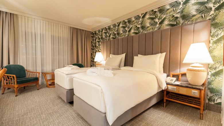 Hotelzimmer mit zwei Einzelbetten, tropischer Tapete und Nachttischlampen.