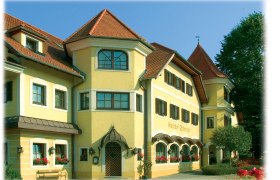 Gelbes Gebäude mit roten Dächern und vielen Fenstern, umgeben von Bäumen.