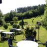 Garten mit Tischen und St&uuml;hlen, umgeben von B&auml;umen und Wiesen.