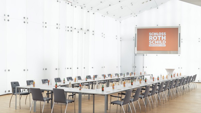 Moderner Konferenzraum im Schloss Rothschild mit langen Tischen, Stühlen und Getränken.