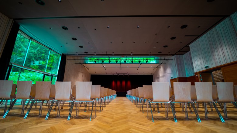 Innenansicht eines modernen Veranstaltungsraums mit leeren Stuhlreihen und einer B&uuml;hne im Hintergrund.