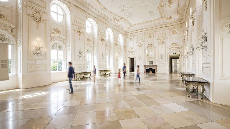 Großer, heller Festsaal mit hohen Fenstern und verzierten Wänden im Schloss Hof.