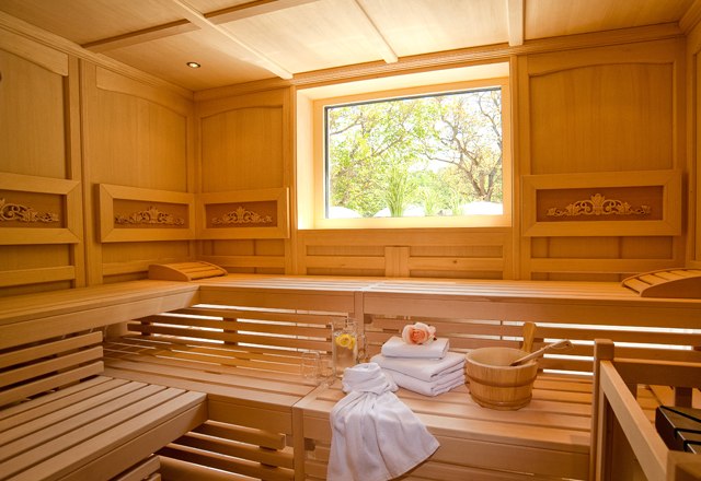 Innenansicht einer Sauna mit Holzb&auml;nken, Handt&uuml;chern und einem Fenster mit Blick ins Gr&uuml;ne.