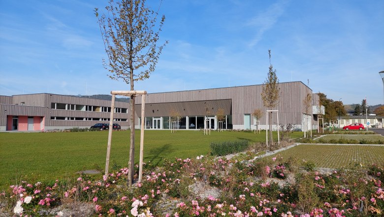 Moderne Gebäude mit Holzfassade und gepflegter Gartenanlage im Vordergrund.