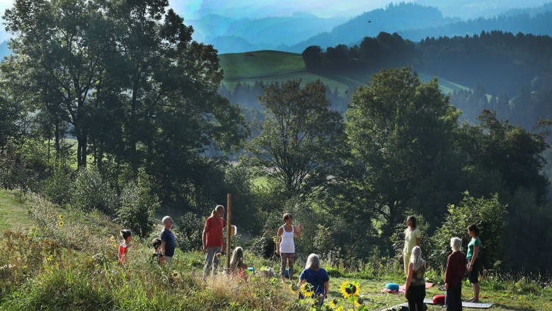 Gruppe von Menschen macht Yoga im Freien vor einer malerischen Berglandschaft.