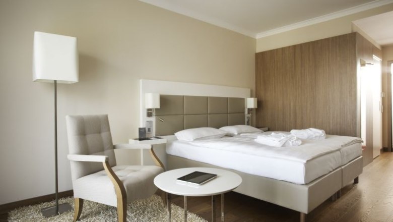 Modernes Hotelzimmer mit Doppelbett, Sessel, Tisch und Stehlampe.