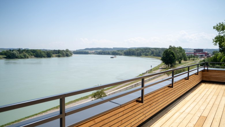 Holzterrasse mit Blick auf einen Fluss und gr&uuml;ne Landschaft.