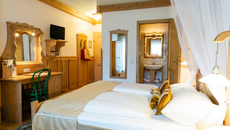 Gem&uuml;tliches Hotelzimmer mit Doppelbett, Holzm&ouml;beln und kleinem Badezimmer.