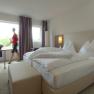 Modern eingerichtetes Hotelzimmer mit Doppelbett, großem Fenster und einer Person, die vorbeigeht.