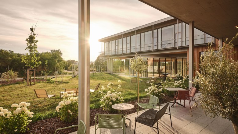 Moderne Terrasse mit Gartenm&ouml;beln und Blumen vor einem Geb&auml;ude bei Sonnenuntergang.