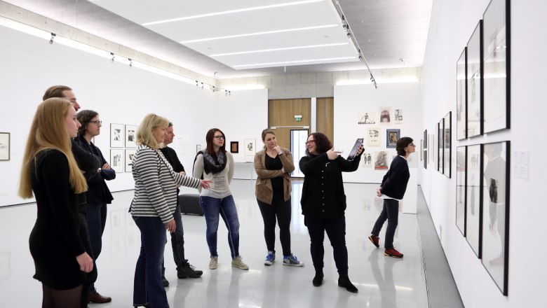 Gruppe von Menschen in einer Kunstgalerie, die Kunstwerke an der Wand betrachten.