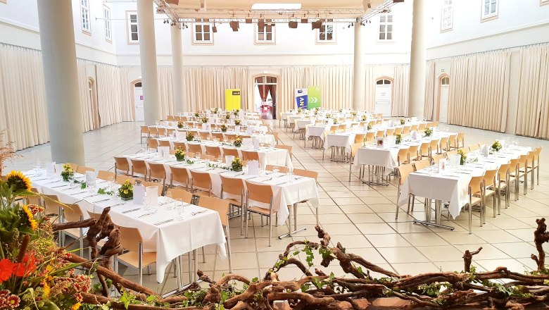 Ein festlich dekorierter Saal mit gedeckten Tischen und Blumenschmuck im Atrium Tulln.